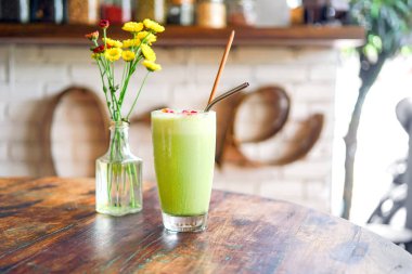 Yeşil matcha çay şeffaf bir vazoda sarı çiçekler ile ahşap bir tabloda boba veya bobble. Arkadaki bulanık bir arka plan beyaz bir tuğla ile bir kelime - seviyorum. Bali Restoran. Yan görünümü kopya alanı