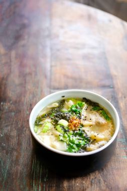 Mantarlı tavuk Mantı çorbası siyah plaka ve ahşap bir masa. Çin yemeği. Masanın üstünde çiçekler şeffaf bir vazo ve yeşil yaprakları ile Lila bir pot vardır. Kopya alanı ile Üstten Görünüm. 