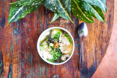 Mantarlı tavuk Mantı çorbası siyah plaka ve ahşap bir masa. Çin yemeği. Masanın üstünde çiçekler şeffaf bir vazo ve yeşil yaprakları ile Lila bir pot vardır. Kopya alanı ile Üstten Görünüm. 