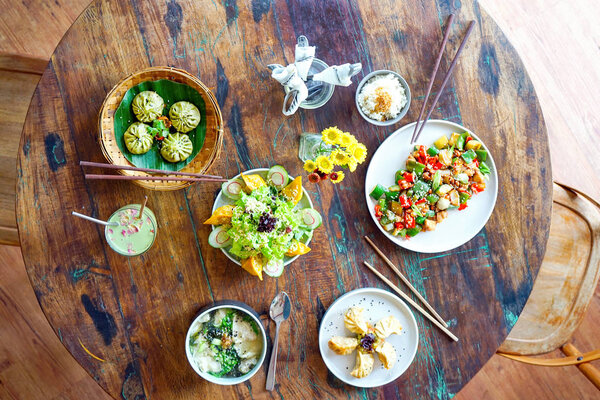 Салат из лосося и грибной куриный суп Вонтон и куриный конг пао на белой тарелке и на деревянном столе. Китайская еда. Женская рука с палочками для еды. Вид сверху с пространством для копирования
. 