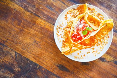 Krep (ya da krep) krem ve olgun çilek ile. Restoranda ahşap bir masaya. Altın gözleme kabuk özenle doldurarak sarılır: çilek, çilek, nane, krem. Üstten Görünüm kopya alanı