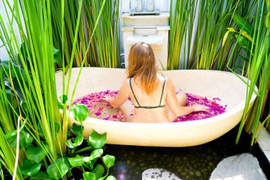 Kızıl saçlı kız çiçek-RIM ile banyoda. Bir kadın bir yuvarlak açık banyo tropik çiçekler, organik cilt bakımı, lüks spa otel Bali Ubud rahatlatır. Kopya alanı ile yan görünüm