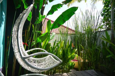 Round outdoor bathroom with frangipani flower petals in an expensive luxury chic and spa hotel in Bali in Ubud, under the feet of swimming carp. Tropical plants and white chaise longue rocking chair clipart