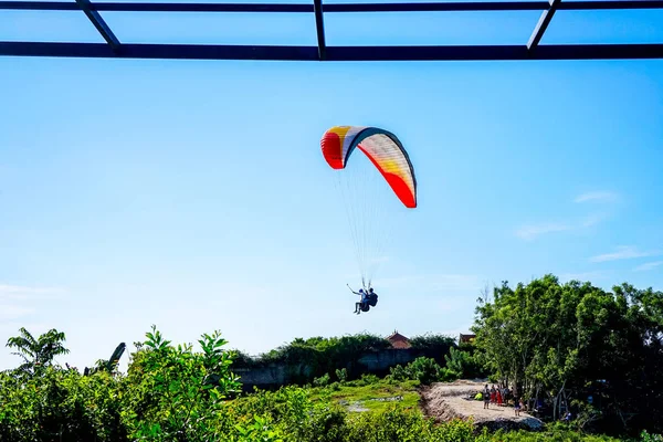 Paragliding over the ocean on the island of Bali. The blue sky shimmers with the blue ocean. The parasutists fly high above the precipice like birds. Aerial view with copy space