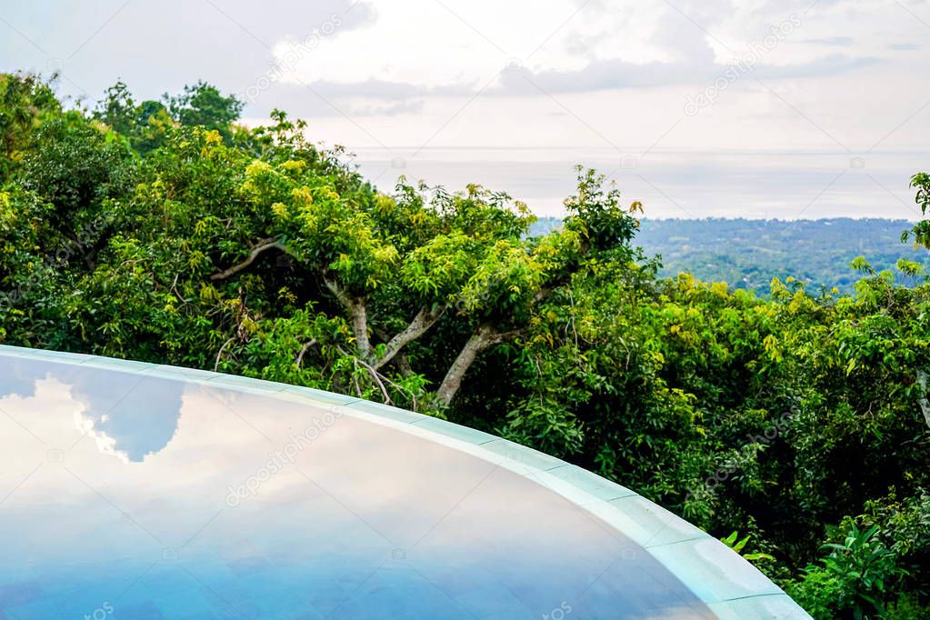 View of the beach shoreline. In the foreground, trees and sky are reflected in the pool. Island of Bali, Lovina beach. Side view with copy space