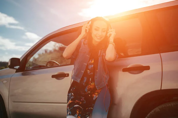 Mujer joven con auriculares posando cerca de coche —  Fotos de Stock