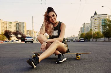 Dövmeli güzel genç kız longboard üzerinde oturur