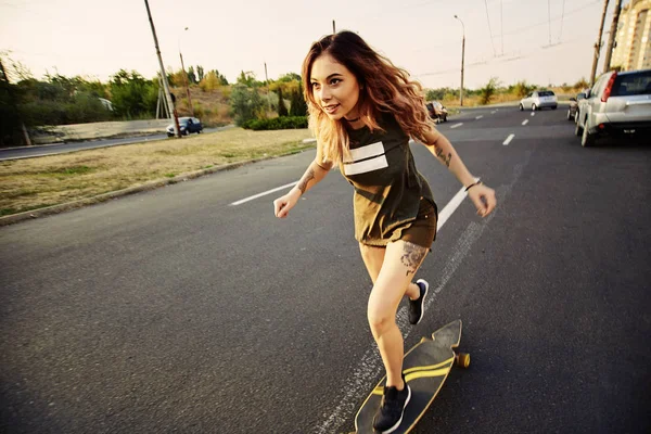 Mooi jong meisje met tatoeages longboard in zonnig weer Paardrijden — Stockfoto