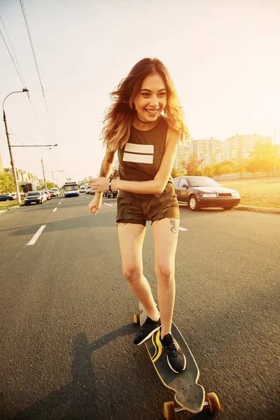 Krásná mladá dívka s tetováním na koni longboard za slunečného počasí — Stock fotografie