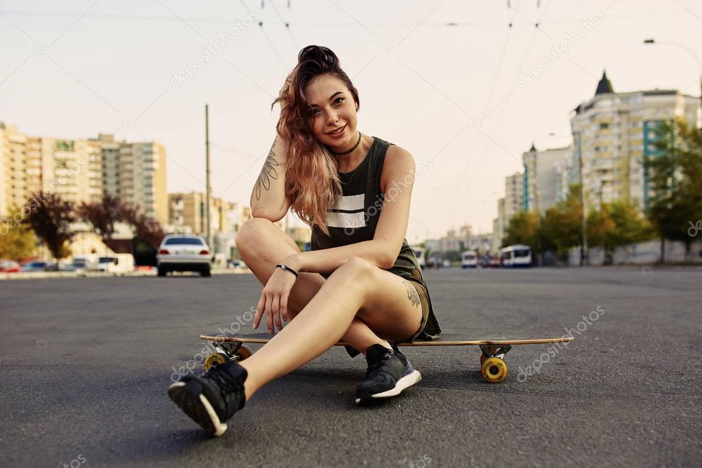 Beautiful young girl with tattoos sits on longboard