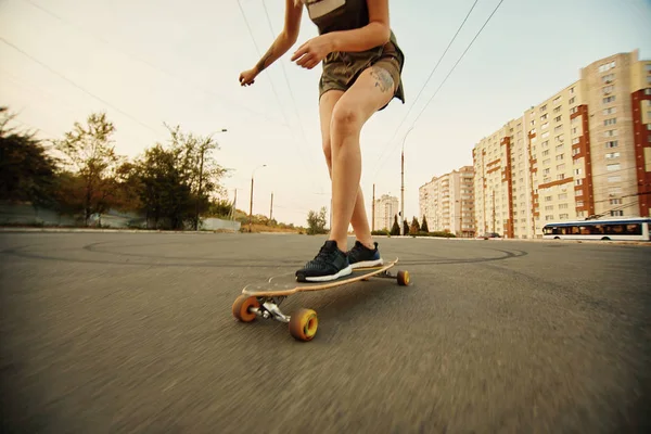 Beautiful young girl with tattoos riding longboard in sunny weather — Stock Photo, Image
