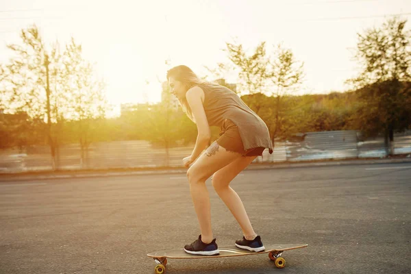 Schönes junges Mädchen mit Tattoos beim Longboard-Reiten bei sonnigem Wetter — Stockfoto