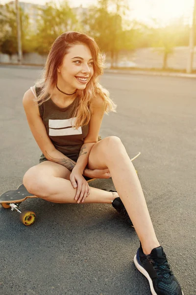 Piękna młoda dziewczyna z tatuażami siedzi na longboard — Zdjęcie stockowe