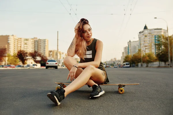 Hermosa chica joven con tatuajes se sienta en longboard — Foto de Stock