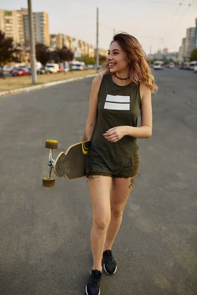 Mooie jonge getatoeëerd meisje met longboard bij zonnig weer — Stockfoto