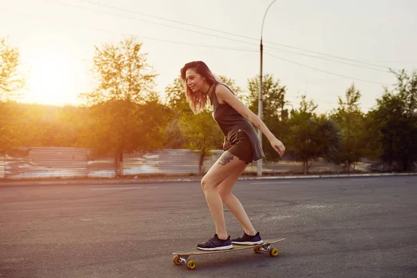 Krásná mladá dívka s tetováním na koni longboard za slunečného počasí — Stock fotografie