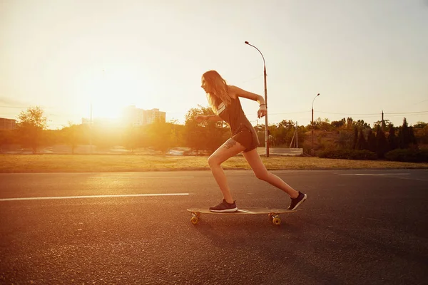 Schönes junges Mädchen mit Tattoos beim Longboard-Reiten bei sonnigem Wetter — Stockfoto