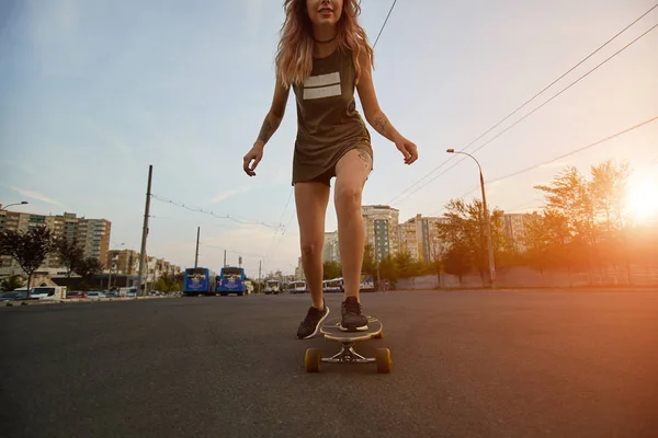 Schönes junges Mädchen mit Tattoos beim Longboard-Reiten bei sonnigem Wetter — Stockfoto