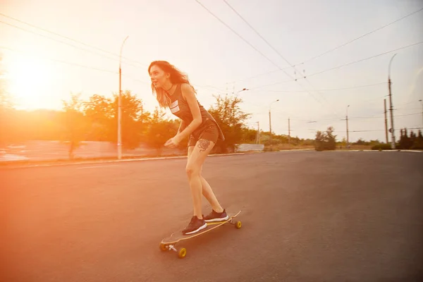 Szép fiatal lány lovaglás longboard napos időben tetoválás — Stock Fotó