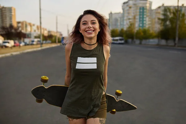 Schönes Mädchen mit Tätowierungen posiert mit einem bunten Longboard — Stockfoto
