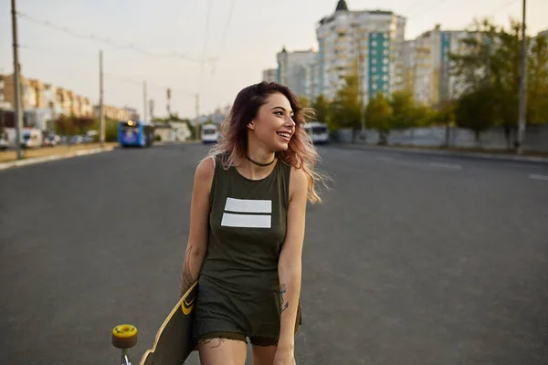 Vacker flicka med tatueringar poserar med en färgglad longboard — Stockfoto