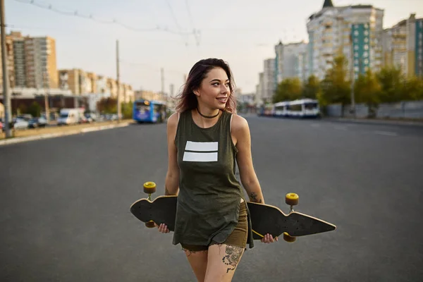 Mooi meisje met tatoeages poseren met een kleurrijke longboard — Stockfoto