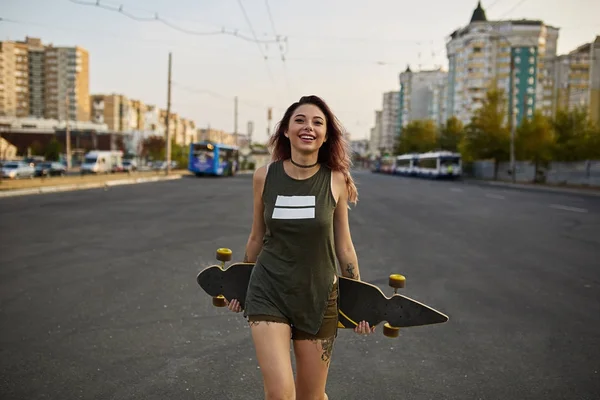 Beautiful girl with tattoos posing with a colorful longboard — Stock Photo, Image