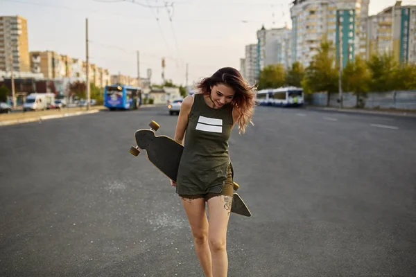 Schönes Mädchen mit Tätowierungen posiert mit einem bunten Longboard — Stockfoto