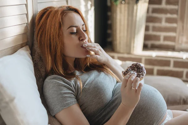 Těhotná žena jíst chutné koblihy — Stock fotografie