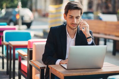 Genç girişimci dizüstü bilgisayar ve telefon üzerinde çalışıyor