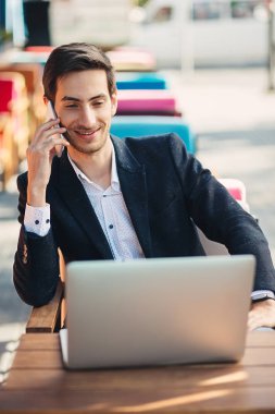 Genç girişimci dizüstü bilgisayar ve telefon üzerinde çalışıyor
