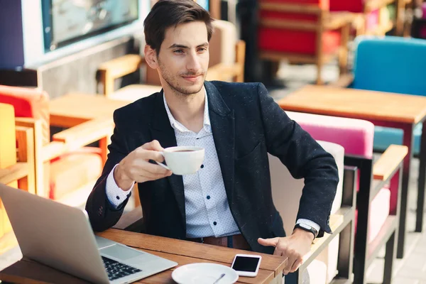 Joven hombre guapo disfrutar del café trabajando en el ordenador portátil — Foto de Stock
