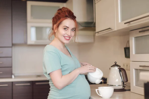 Sorridente donna incinta versando il tè — Foto Stock