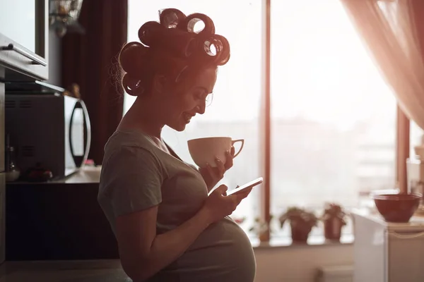 Pregnant woman using smartphone standing near window