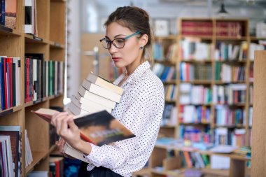 Kitaplıktaki kitapların bir yığınına olan kadın