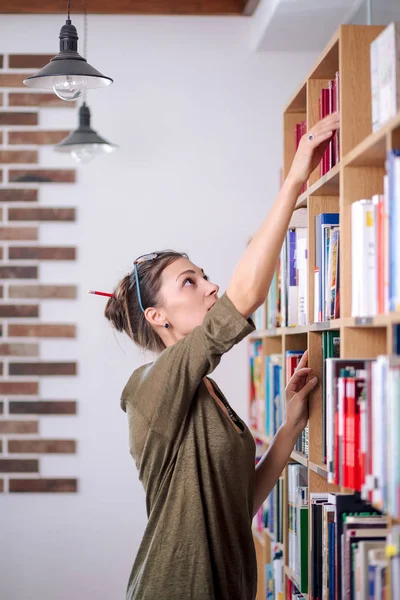 Giovane donna con gli occhiali in cerca di un libro su una libreria, io — Foto Stock