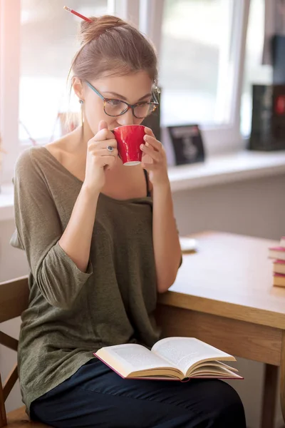 Donna con gli occhiali che legge un libro che beve una tazza di caffè — Foto Stock