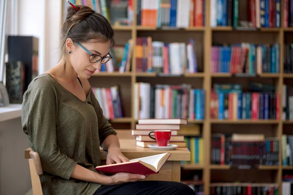Genç güzel kadın bir kütüphane ile bir fincan bir kitap okuma 