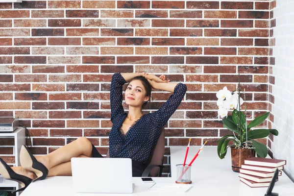 Relaxed business woman with legs on the desk in office smiling