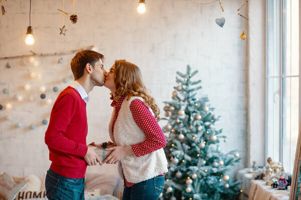Young couple kissing while holding together a present box, with Christmas decorations in background
