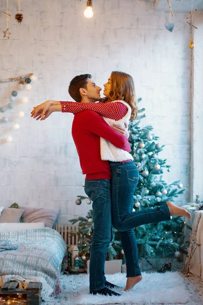 Bild zeigt ein junges Paar, das sich über dem Weihnachtsbaum umarmt und küsst, in voller Länge — Stockfoto