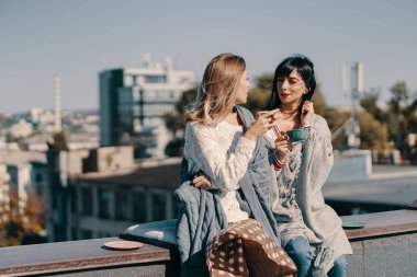 İki çekici kız şehre tepeden bakan bir çatıda çay partisinin tadını çıkarıyor.
