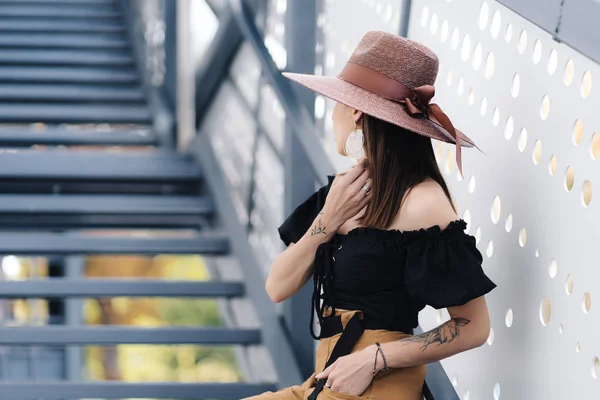 Mulher morena elegante com cabelo longo, vestindo chapéu de vime grande elegante, posando nas escadas — Fotografia de Stock