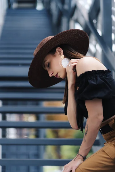 Modieuze brunette vrouw met lang haar, dragen stijlvolle grote rieten hoed, poseren op de trap — Stockfoto