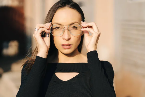 Привлекательная юная брюнетка в черном топе и прозрачных очках, позирующих на улице — стоковое фото