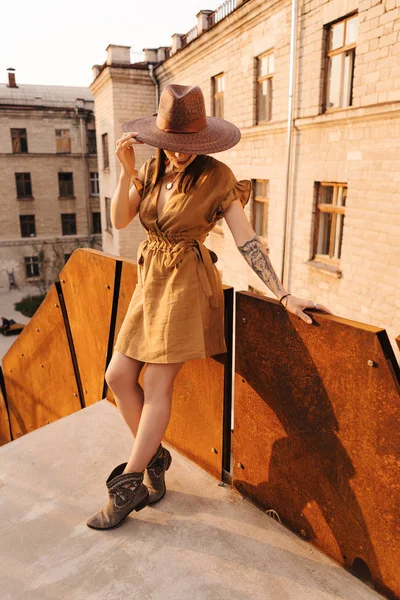 Young fashion girl dressed in a summer dress with a wicker wide hat walks and poses in the old city — Stock Photo, Image