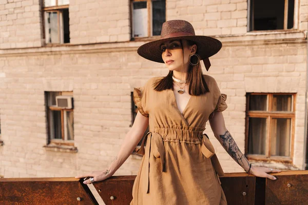 Menina de moda jovem vestida em um vestido de verão com um chapéu largo de vime caminha e posa na cidade velha — Fotografia de Stock