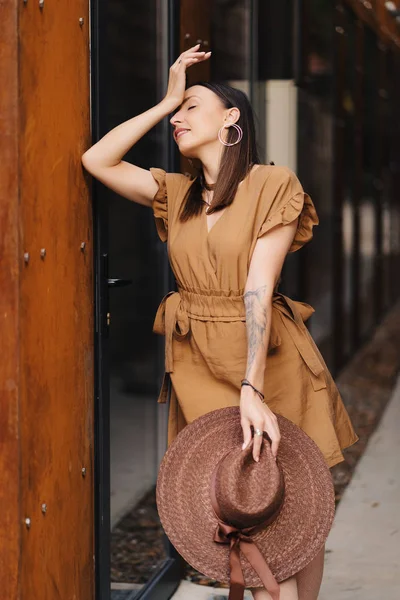 Jeune fille de la mode vêtue d'une robe d'été avec un chapeau large en osier marche et pose dans la vieille ville — Photo