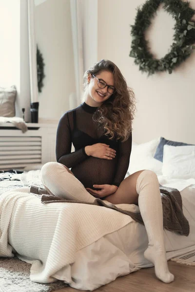 Människor känslor, väntar på ett nytt liv. Ung, vacker kvinna njuter av sin graviditet och feminina kropp samtidigt röra magen sitter på sängen hemma — Stockfoto