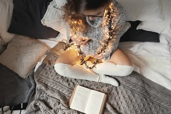 Young future mom sending positive vibes to her unborn child by reading and decorating her clothes with lights — 스톡 사진